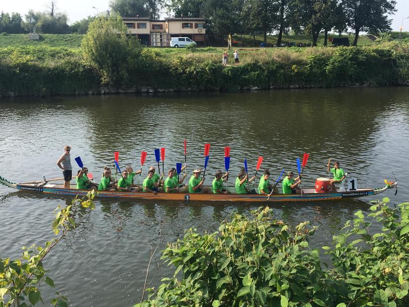 Na zdjęciu jedna ze smoczych łodzi z załogą w zielonych koszulkach na rzece. 